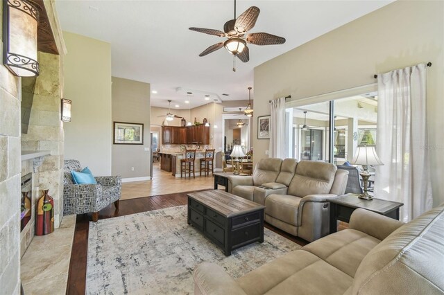 living room featuring ceiling fan, a stone fireplace, a wealth of natural light, and light wood-type flooring