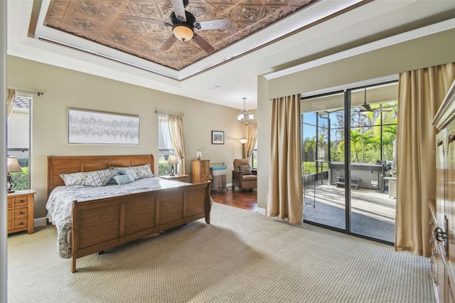 carpeted bedroom featuring a tray ceiling, access to exterior, ceiling fan with notable chandelier, and crown molding