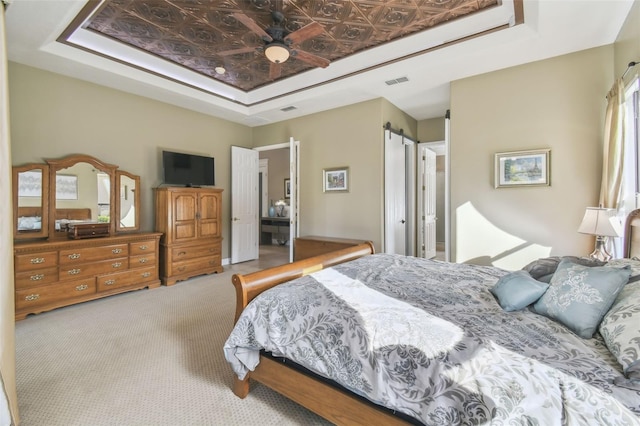 bedroom featuring a raised ceiling, a barn door, and light colored carpet