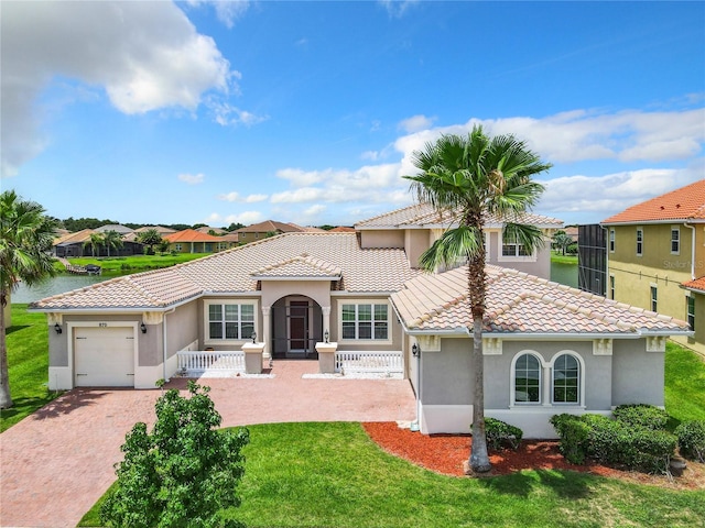 mediterranean / spanish home with a garage, a front lawn, and a water view