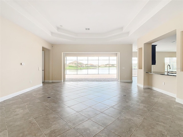 tiled empty room featuring a water view, sink, and a tray ceiling