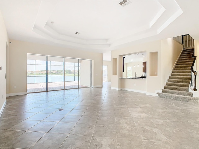 unfurnished living room with a water view, light tile patterned floors, and a raised ceiling