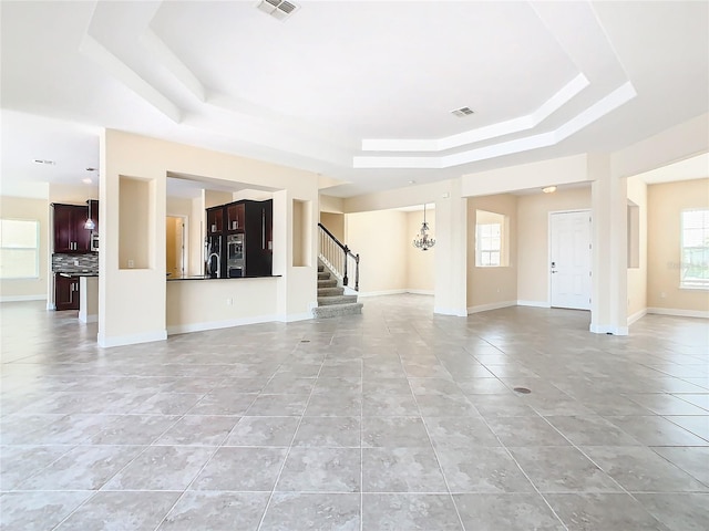 unfurnished living room with an inviting chandelier, light tile patterned flooring, and a tray ceiling