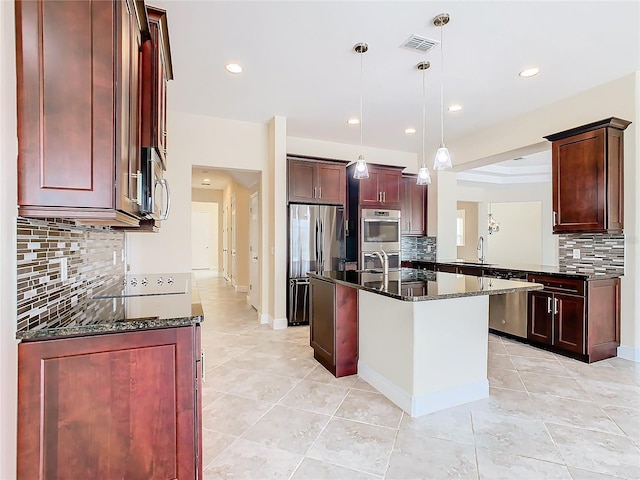 kitchen featuring appliances with stainless steel finishes, dark stone counters, sink, hanging light fixtures, and a kitchen island with sink