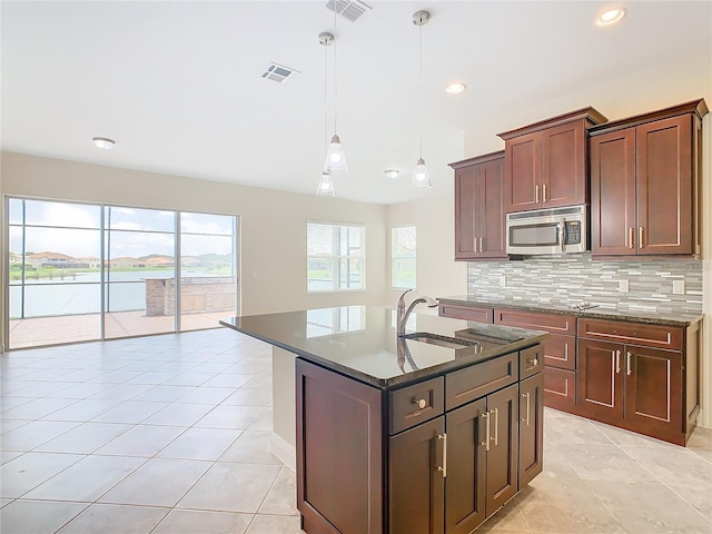 kitchen featuring decorative light fixtures, an island with sink, sink, backsplash, and light tile patterned flooring