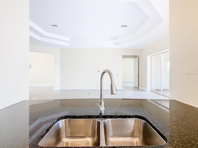 kitchen featuring a raised ceiling, dark stone counters, and sink