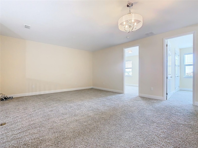 carpeted empty room featuring a healthy amount of sunlight and an inviting chandelier