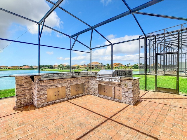 view of patio / terrace featuring a lanai, exterior kitchen, a water view, and grilling area