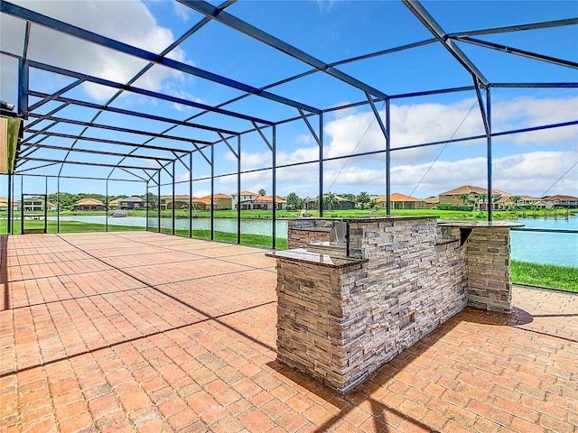 view of patio featuring glass enclosure, a water view, exterior kitchen, and exterior bar