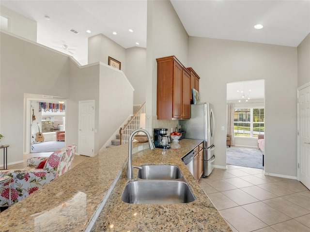 kitchen with sink, light stone counters, light tile patterned floors, appliances with stainless steel finishes, and a towering ceiling