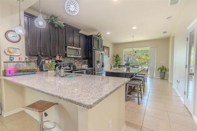 kitchen featuring light tile patterned floors, visible vents, appliances with stainless steel finishes, backsplash, and a kitchen bar