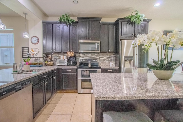 kitchen featuring light tile patterned floors, backsplash, light stone countertops, stainless steel appliances, and a sink