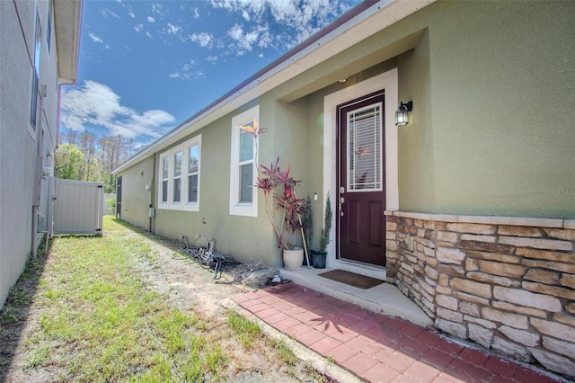 property entrance with stone siding, fence, and stucco siding