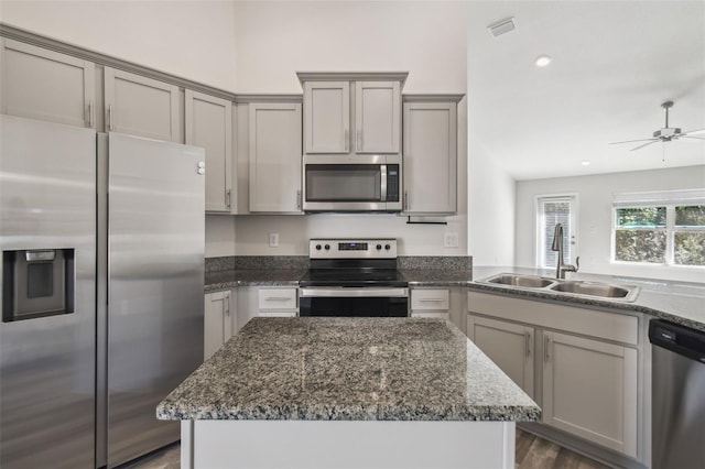 kitchen with sink, appliances with stainless steel finishes, dark stone countertops, a center island, and dark hardwood / wood-style flooring