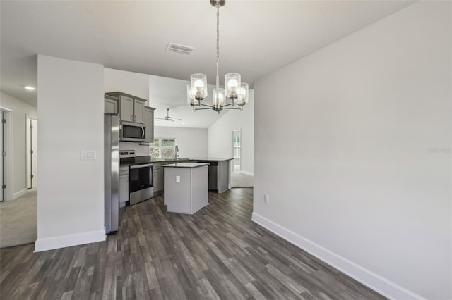 kitchen featuring appliances with stainless steel finishes, a chandelier, hanging light fixtures, a center island, and dark wood-type flooring