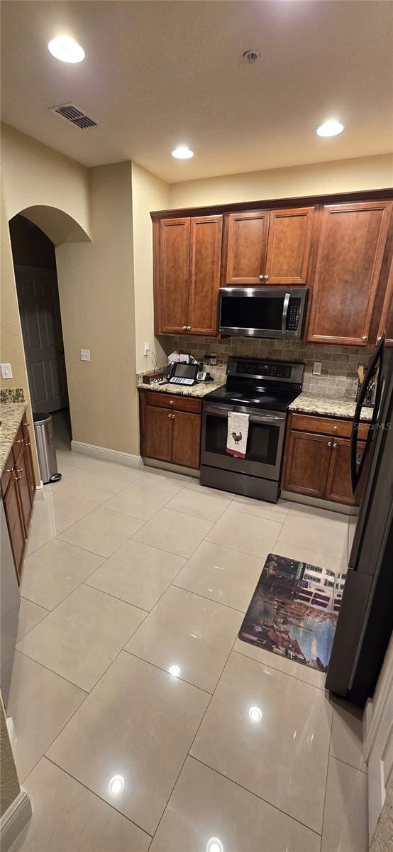 kitchen featuring light tile patterned floors, stainless steel appliances, backsplash, and light stone countertops