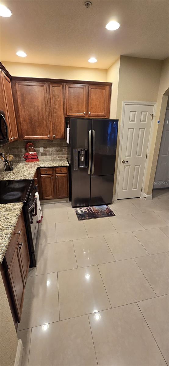 kitchen with black appliances, light tile patterned floors, decorative backsplash, and light stone countertops