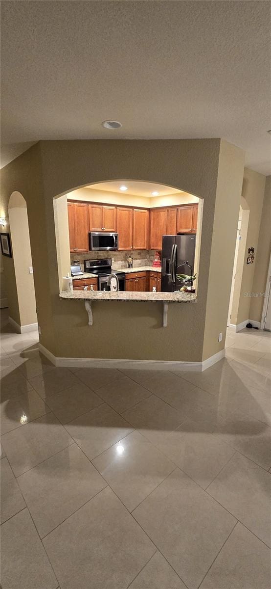 kitchen with a kitchen bar, appliances with stainless steel finishes, and light tile patterned flooring