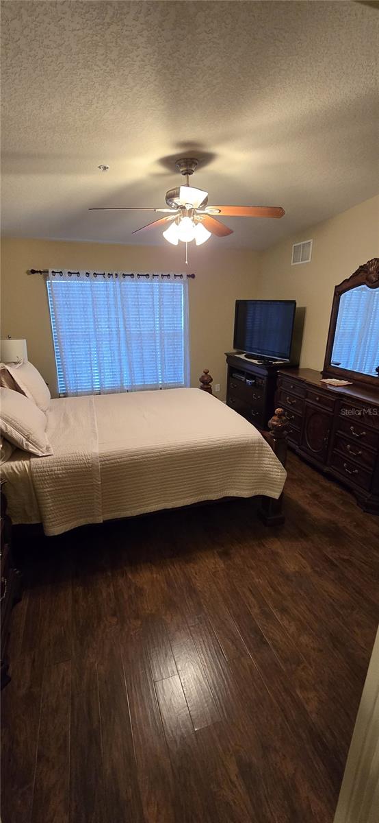 bedroom with ceiling fan, dark hardwood / wood-style floors, and a textured ceiling