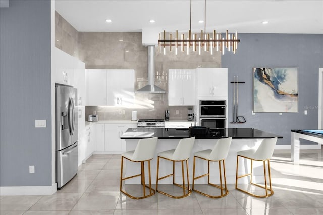 kitchen with pendant lighting, appliances with stainless steel finishes, wall chimney exhaust hood, white cabinetry, and a center island