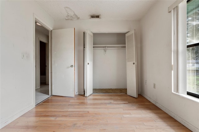 unfurnished bedroom featuring a textured ceiling, a closet, and light hardwood / wood-style flooring