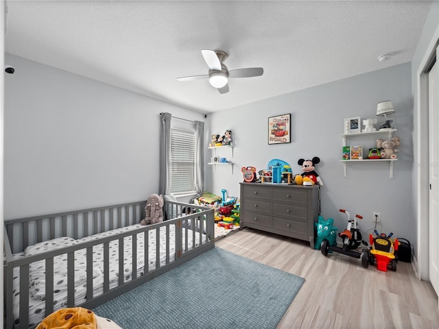 bedroom with ceiling fan, a crib, and light hardwood / wood-style flooring