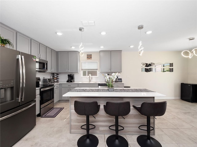 kitchen featuring appliances with stainless steel finishes, gray cabinetry, a kitchen island, and decorative light fixtures