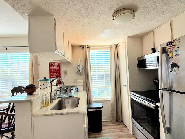 kitchen with appliances with stainless steel finishes, white cabinets, sink, light hardwood / wood-style flooring, and kitchen peninsula