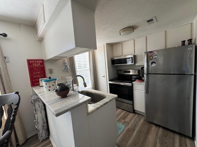 kitchen with appliances with stainless steel finishes, a textured ceiling, sink, kitchen peninsula, and dark hardwood / wood-style flooring