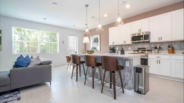 kitchen featuring white cabinetry, an island with sink, appliances with stainless steel finishes, tasteful backsplash, and pendant lighting