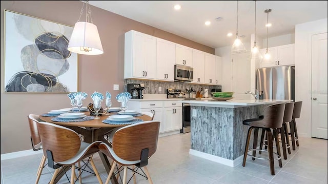 kitchen featuring white cabinetry, appliances with stainless steel finishes, decorative backsplash, decorative light fixtures, and a kitchen island with sink