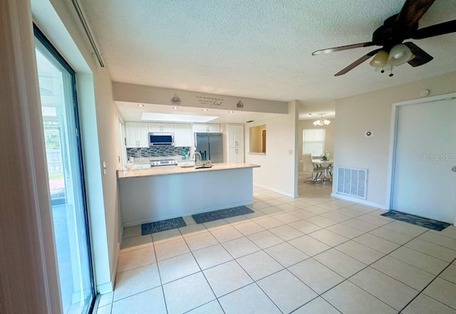 kitchen featuring white cabinetry, kitchen peninsula, appliances with stainless steel finishes, decorative backsplash, and light tile patterned flooring