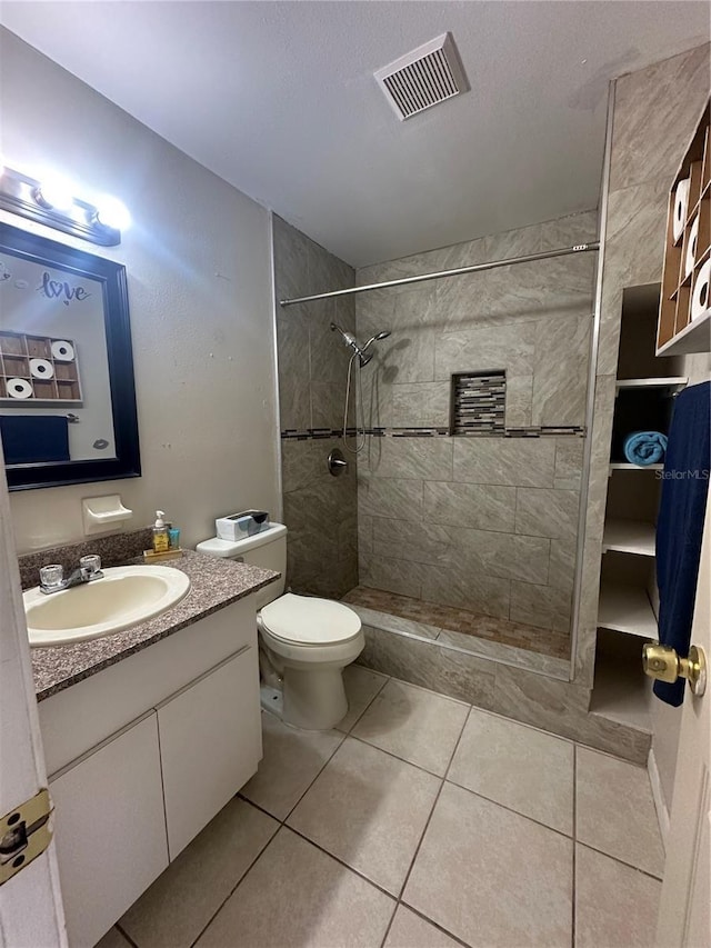 bathroom with toilet, tile patterned flooring, a tile shower, and vanity