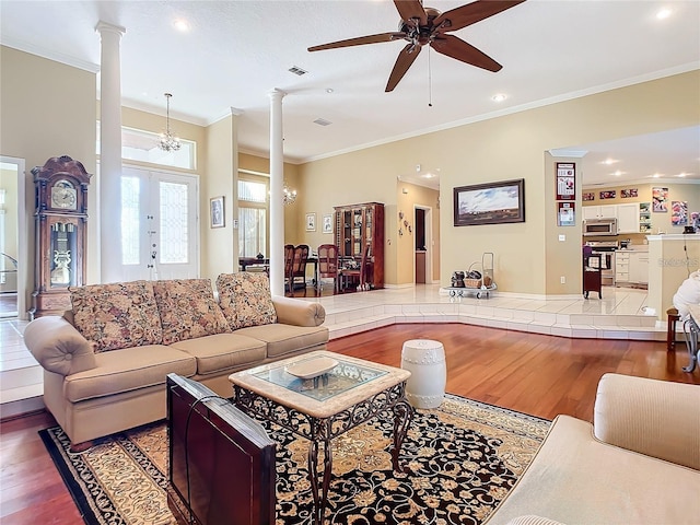 living room with decorative columns, hardwood / wood-style flooring, ceiling fan with notable chandelier, and crown molding