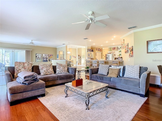 living room featuring wood-type flooring, a textured ceiling, ceiling fan, and ornamental molding