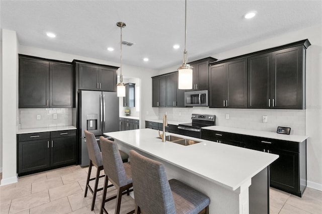 kitchen featuring decorative light fixtures, appliances with stainless steel finishes, sink, and a center island with sink