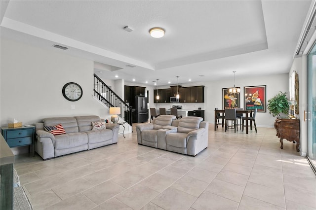 living room with a tray ceiling, light tile patterned floors, and a notable chandelier