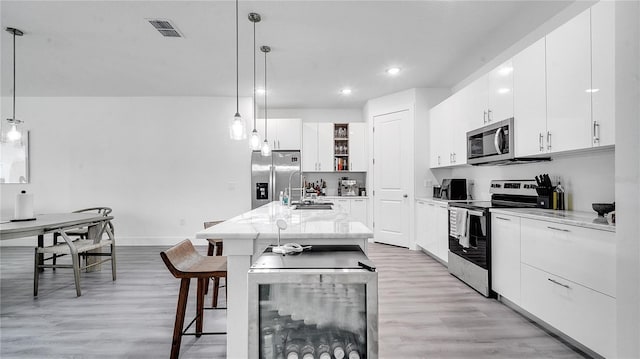 kitchen featuring appliances with stainless steel finishes, a kitchen island with sink, pendant lighting, white cabinets, and a breakfast bar