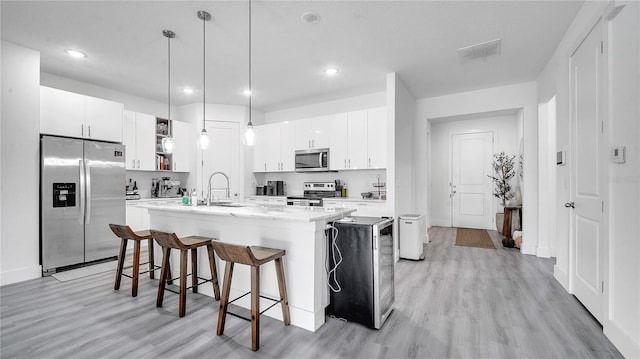 kitchen with decorative light fixtures, an island with sink, stainless steel appliances, and white cabinetry