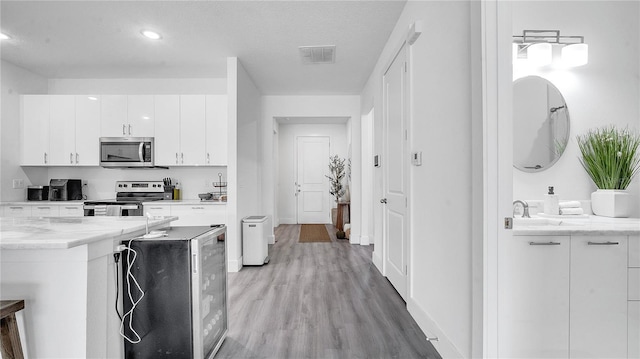 kitchen with a textured ceiling, white cabinets, beverage cooler, appliances with stainless steel finishes, and light wood-type flooring