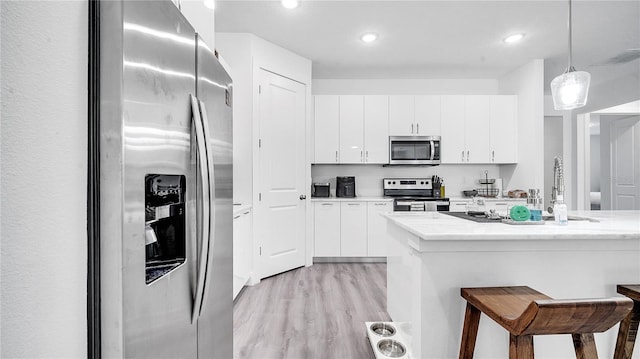 kitchen with stainless steel appliances, decorative light fixtures, light wood-type flooring, white cabinets, and a breakfast bar