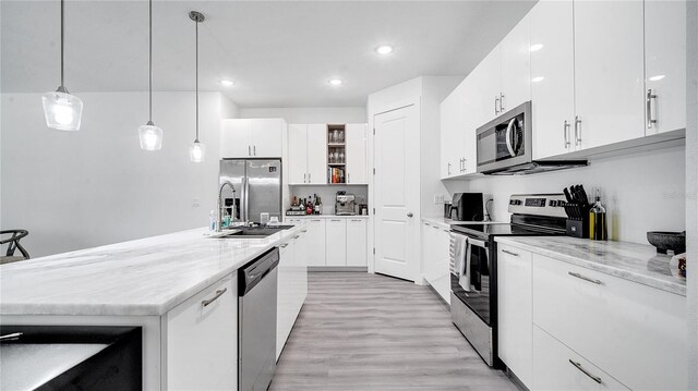 kitchen featuring stainless steel appliances, white cabinetry, hanging light fixtures, and light stone countertops