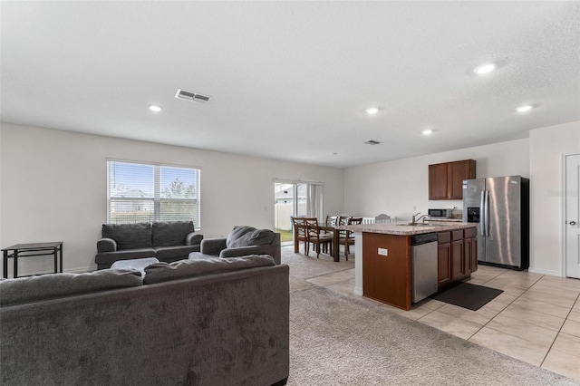 kitchen with appliances with stainless steel finishes, an island with sink, sink, light carpet, and a textured ceiling