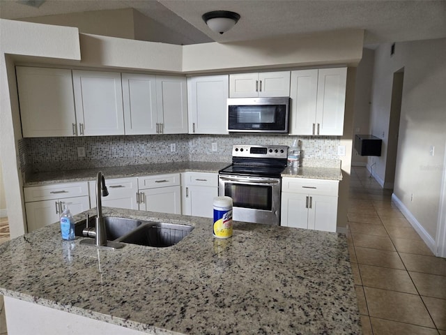 kitchen featuring white cabinetry, appliances with stainless steel finishes, lofted ceiling, light stone countertops, and sink