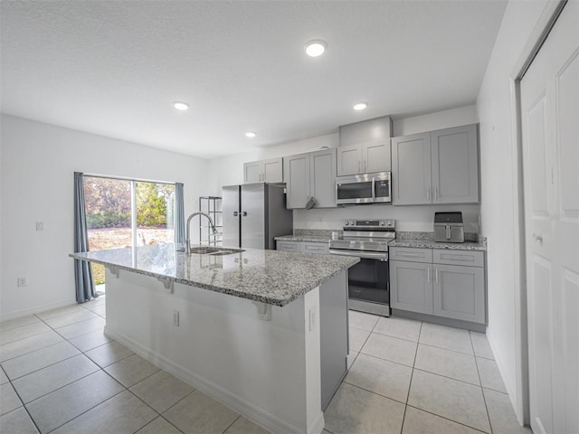 kitchen featuring appliances with stainless steel finishes, gray cabinetry, an island with sink, and sink