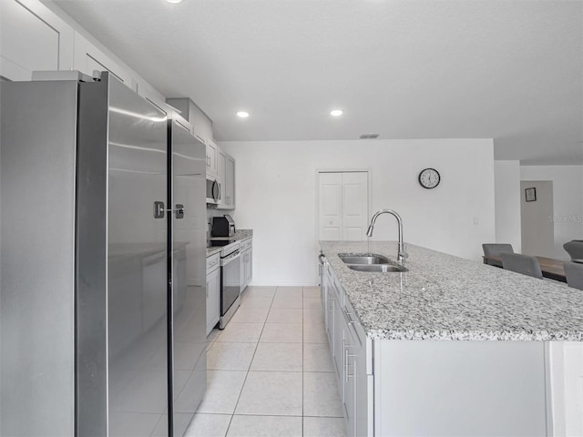 kitchen with sink, white cabinetry, a kitchen island with sink, stainless steel appliances, and light tile patterned floors