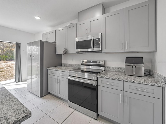 kitchen with light stone countertops, gray cabinets, stainless steel appliances, and light tile patterned flooring