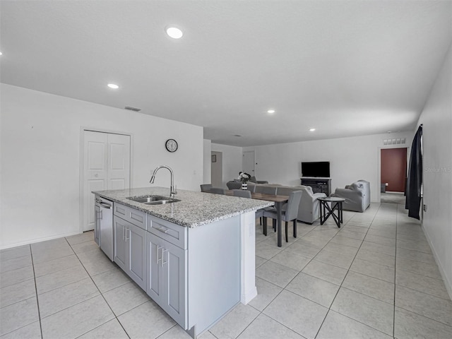 kitchen with an island with sink, gray cabinetry, sink, and light stone counters