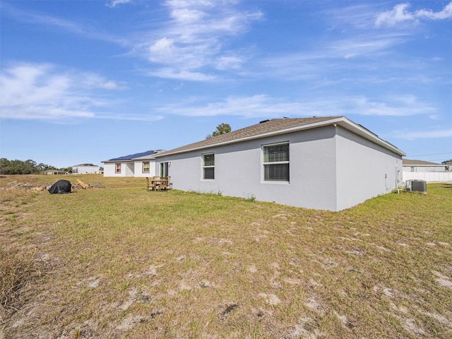 rear view of property with central AC unit and a lawn