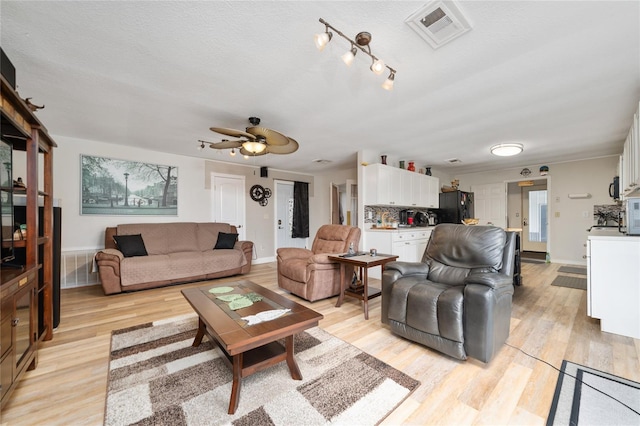 living room featuring light wood-type flooring, ceiling fan, and a textured ceiling